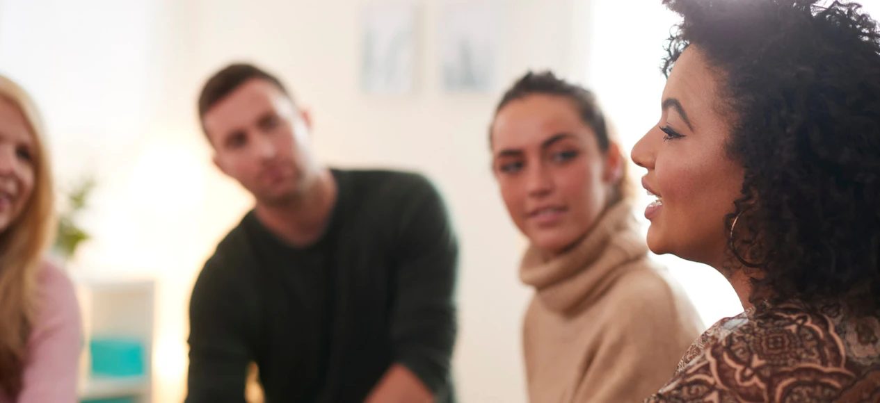 A small group seated in a circle, listening as one person speaks