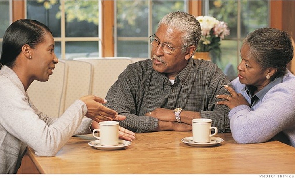 Image of three African-American family members sitting at table with coffee cups. Middle-aged daughter is talking to her elderly mother and father.